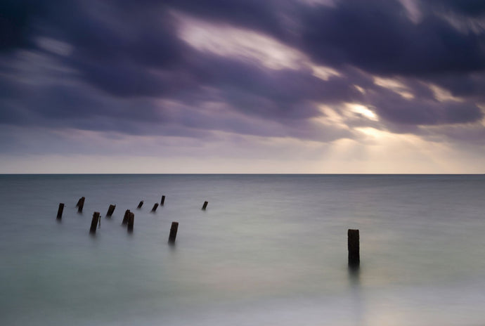 Wooden posts in sea under stormy sky at sunrise, Placencia, Stann Creek, Belize