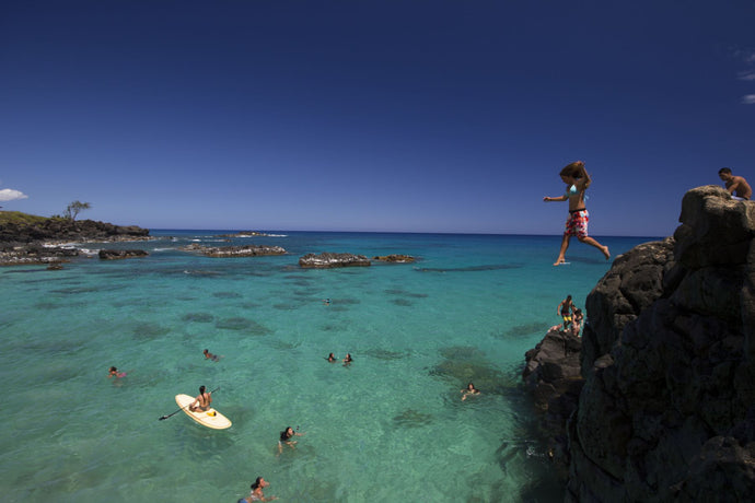 Woman jumping from rocks into the ocean, Hawaii, USA